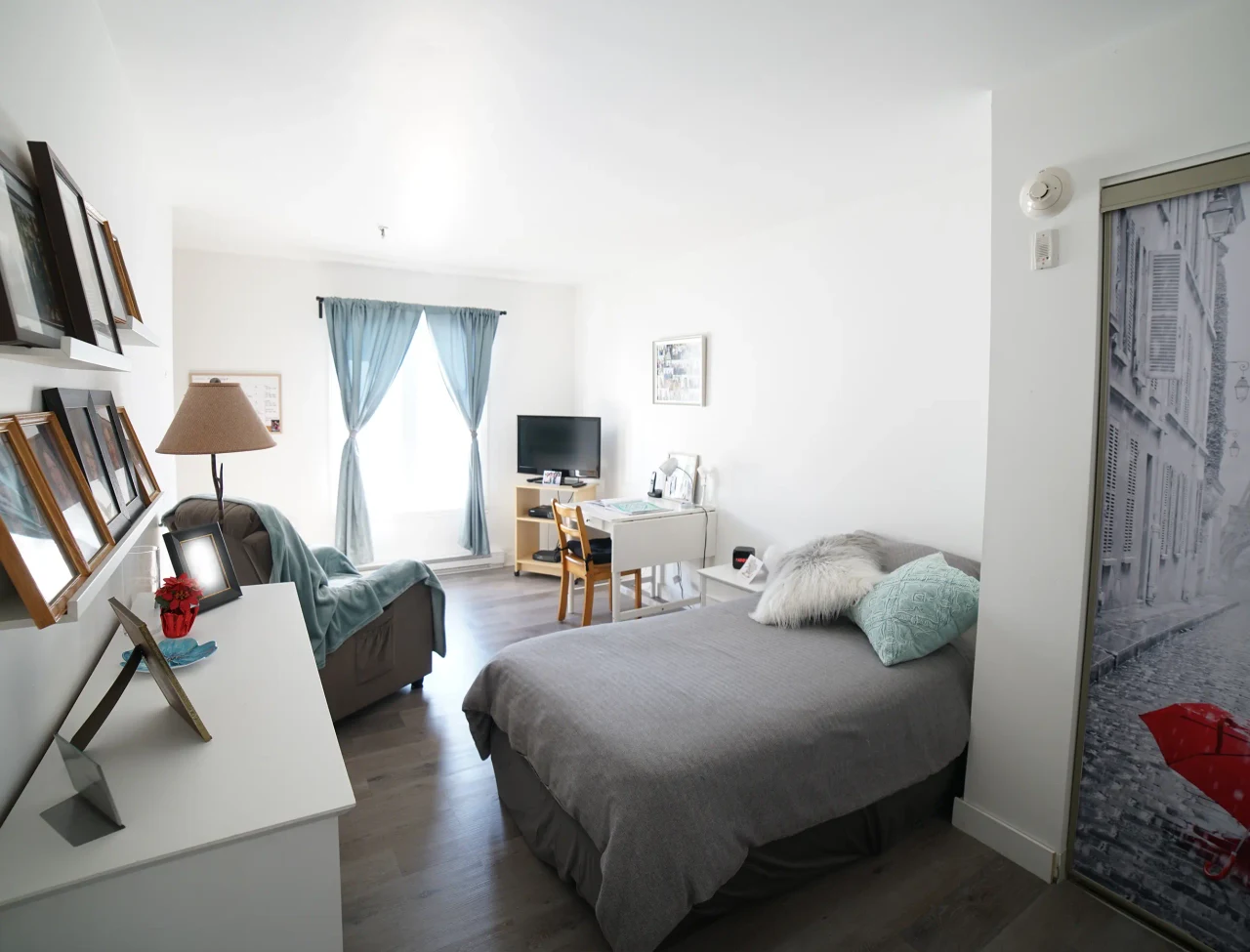 Une chambre meublée avec un lit, une bibliothèque et un fauteuil à la Résidence Sainte-Famille